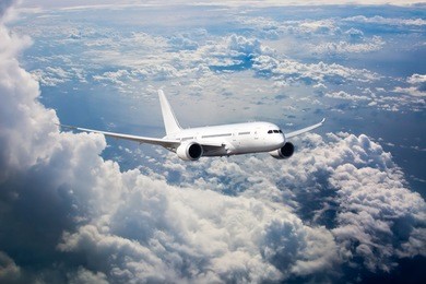 white passenger jet plane in the blue sky. aircraft flying high through the cumulus clouds. airplane front view.