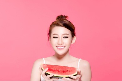healthy asian young woman eat watermelon, this girl really love fruits, she have beauty face and natural makeup, isolated over pink background.