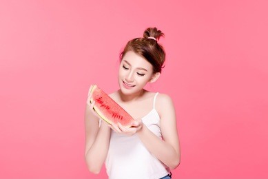 healthy asian young woman eat watermelon, this girl really love fruits, she have beauty face and natural makeup, isolated over pink background.