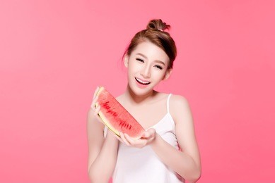 healthy asian young woman eat watermelon, this girl really love fruits, she have beauty face and natural makeup, isolated over pink background.