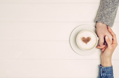 couple in love holding hands with coffee on white wooden table. photograph taken from above, top view with copy space
