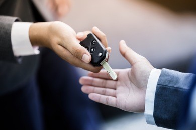 car salesman handing over the keys for a new car to a young businessman