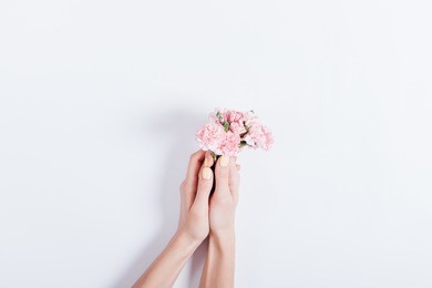 female hands holding a small bouquet of pink flowers on a light background