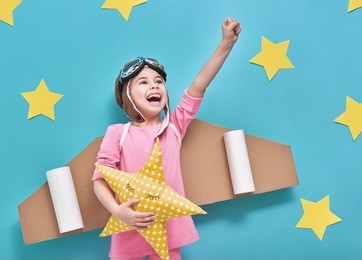 little child girl in an astronaut costume is playing and dreaming of becoming a spaceman. portrait of funny kid on a background of bright blue wall with yellow stars.
