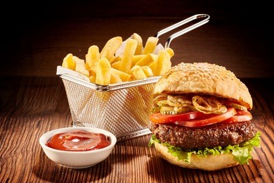 studio shot of high burger with french fries in small fry basket and bowl of ketchup on wooden surface