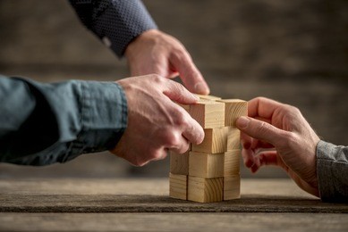 hands of three people building a tower of wood blocks on a table, teamwork concept.