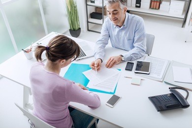 confident advisor meeting with a customer in his office, he is explaining a contract document and policy to the woman sitting at his desk