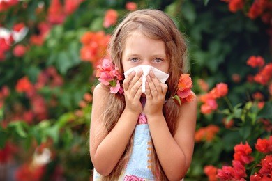 allergy. little girl is blowing her nose near spring tree in bloom. closeup portrait