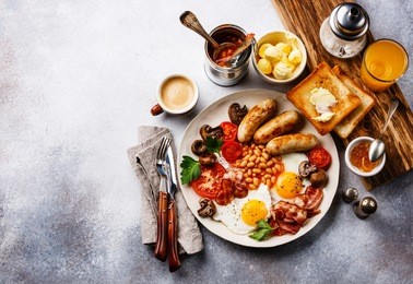 full english breakfast with fried eggs, sausages, bacon, beans, toasts and coffee on copy space background