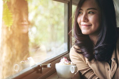 a beautiful asian woman and hot coffee with whipped cream topping in the cafe , feeling happy and smiley face