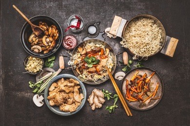 asian food cooking. wok with noodles chicken stir fry and vegetables ingredients with spices ,sauces and chopsticks on dark rustic background, top view