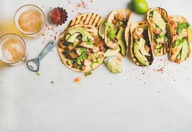 healthy corn tortillas with grilled chicken, avocado, fresh salsa, limes and beer in glasses over light grey marble table background, top view, copy space. gluten-free, allergy-friendly food concept