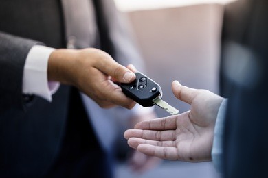 car salesman handing over the keys for a new car to a young businessman