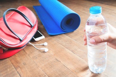 woman hand holding bottle of water with yogamat, baf and phone background