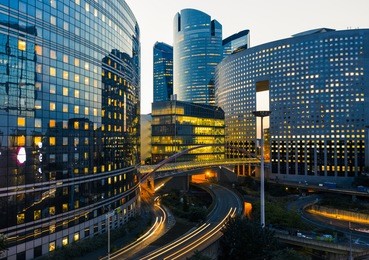 night architecture - skyscrapers with glass facade. modern buildings in paris business district. evening dynamic traffic on a street. concept of economics, financial.  copy space for text. toned