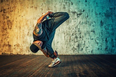 young man break dancing and standing on one leg on wall background. vibrant colors effect. tattoo on body.