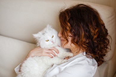 cute girl with curly hair hugging white fluffy cat