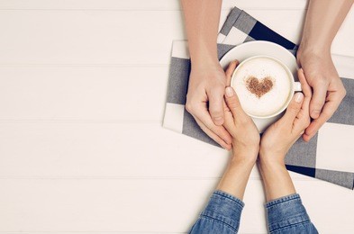 couple in love holding hands with coffee on white wooden table. photograph taken from above, top view with copy space