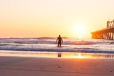 the silhouette of a surfer heading into the water for a surf