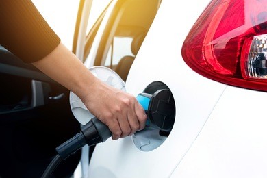 hand holding and charging electric car with the power cable supply plugged in . flare light effect