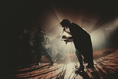 singer / vocalist performing on stage at a concert in the fog. dark background, smoke, concert  spotlights. and saxophone player behind.