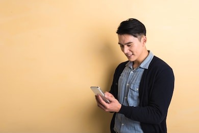 handsome asian young man using smartphone, shot at studio yellow background
