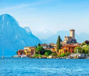 ancient tower and fortress in old town malcesine at garda lake. veneto region. italy. high snowbound top mountains on background. summer landscape with colorful houses green trees.