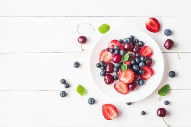 fruit salad with strawberry, blueberry, sweet cherry on wooden white background. flat lay, top view