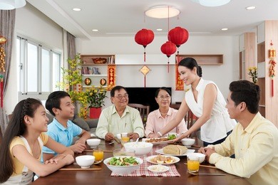 woman bringing main dish to dinner table for tet celebration; couplets with best wishes for coming year in the background