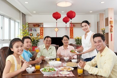 happy vietnamese family having dinner for tet celebration; couplets with best wishes for coming year in the background