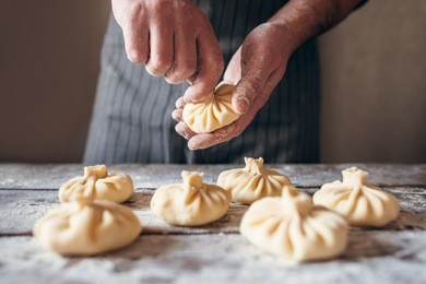 man making khinkali for his family close-up. unrecognizable cook preparing georgian traditional meal of dough and meat at kitchen. national cuisine, cooking process concept