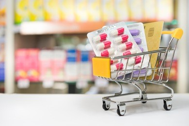 shopping trolley with blisters of medical capsule pills and credit card with blurred medicines shelves in pharmacy shop background