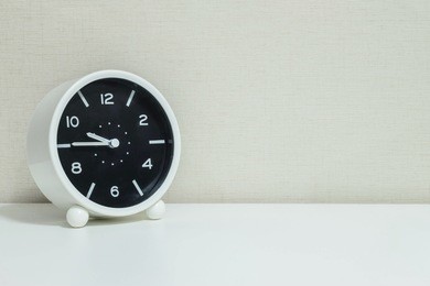 closeup black and white alarm clock for decorate in a quarter to ten or 9:45 a.m. on white wood desk and cream wallpaper textured background with copy space