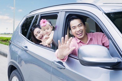 portrait of happy family looking out car window while smiling at the camera in the highway