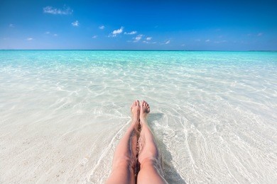 vacation on tropical beach in maldives. woman's legs in the clear ocean water. first person perspective