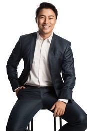 successful and happy entrepreneur in a blue suit and white shirt, sitting down in front of a white background smiling towards camera.