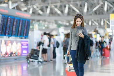 charming beautiful business woman smile in casual style using smartphone with blur the airport terminal.