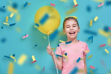 funny child on a background of bright blue wall. girl is having fun with balloons and confetti. yellow, pink and turquoise colors.