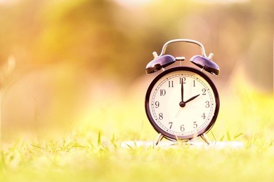 alarm clock on green grass or lawn background, two o'??clock in the afternoon, in the morning - time concept