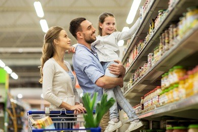 sale, consumerism and people concept - happy family with child and shopping cart buying food at grocery store or supermarket