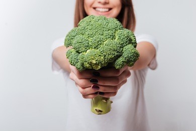 cropped image of young woman dressed in white t-shirt showing broccoli to camera.