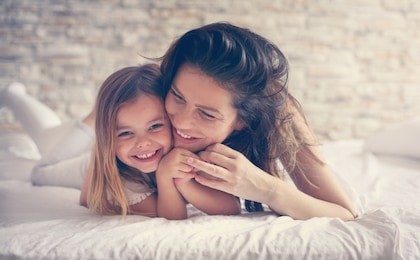 mother and daughter enjoy in bed at home and looking at the camera. 