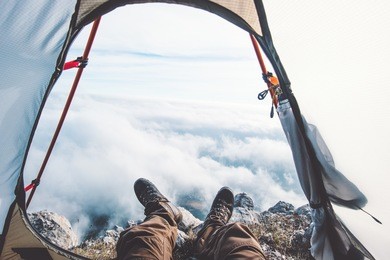 feet man relaxing enjoying clouds mountains aerial view from tent camping entrance outdoor travel lifestyle concept adventure vacations outdoor