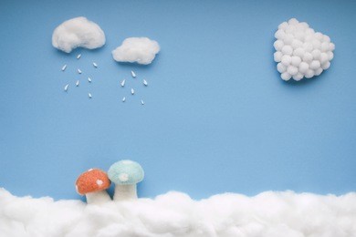 two small clouds pouring rain over two mushrooms and a white heart, in a heavenly scenery where the clouds  are made from cotton-wool, on a blue sky paper background.