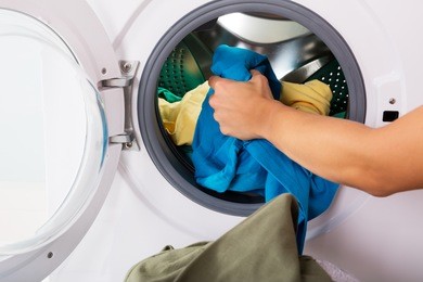 close-up of woman hand loading dirty clothes in washing machine