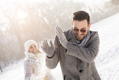young couple playing snowball outdoors on sunny winter day