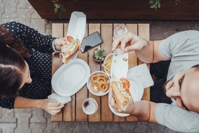 a couple eating hotdogs outdoors
