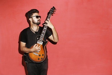 closeup of one handsome passionate expressive cool young brunette rock musician men playing electric guitar standing against red background