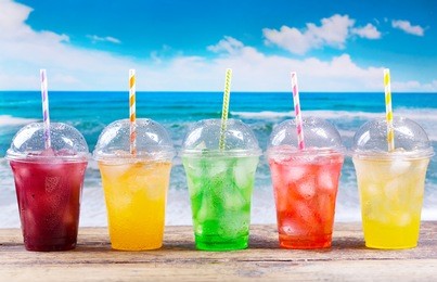 colorful cold drinks in plastic cups with ice on the beach.