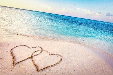 two hearts drawn on sand of a tropical beach at sunset. clear turquoise ocean. maldives islands.